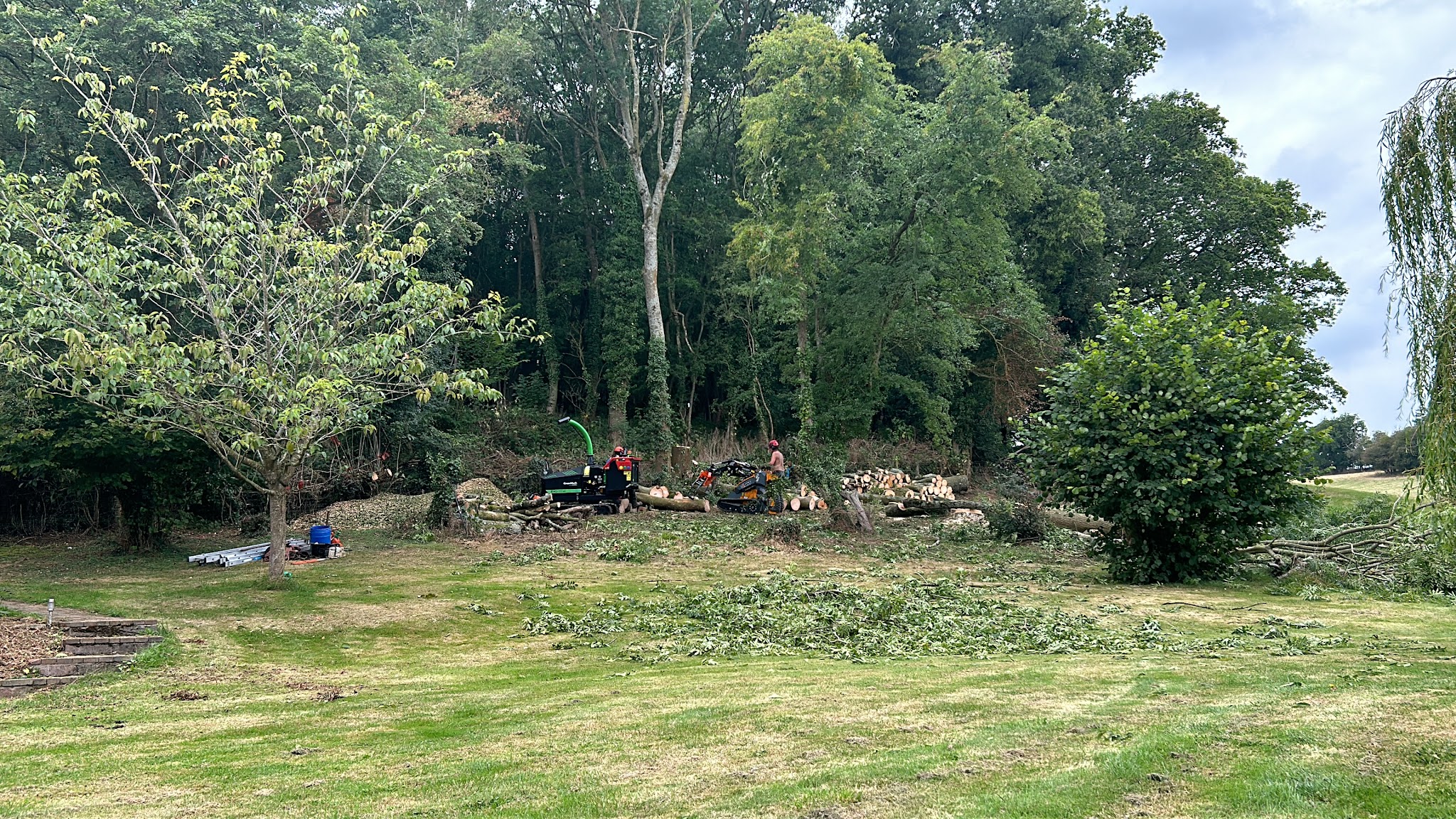 A large lawn cleared after felling, with timber and brash stacked by the woodland edge